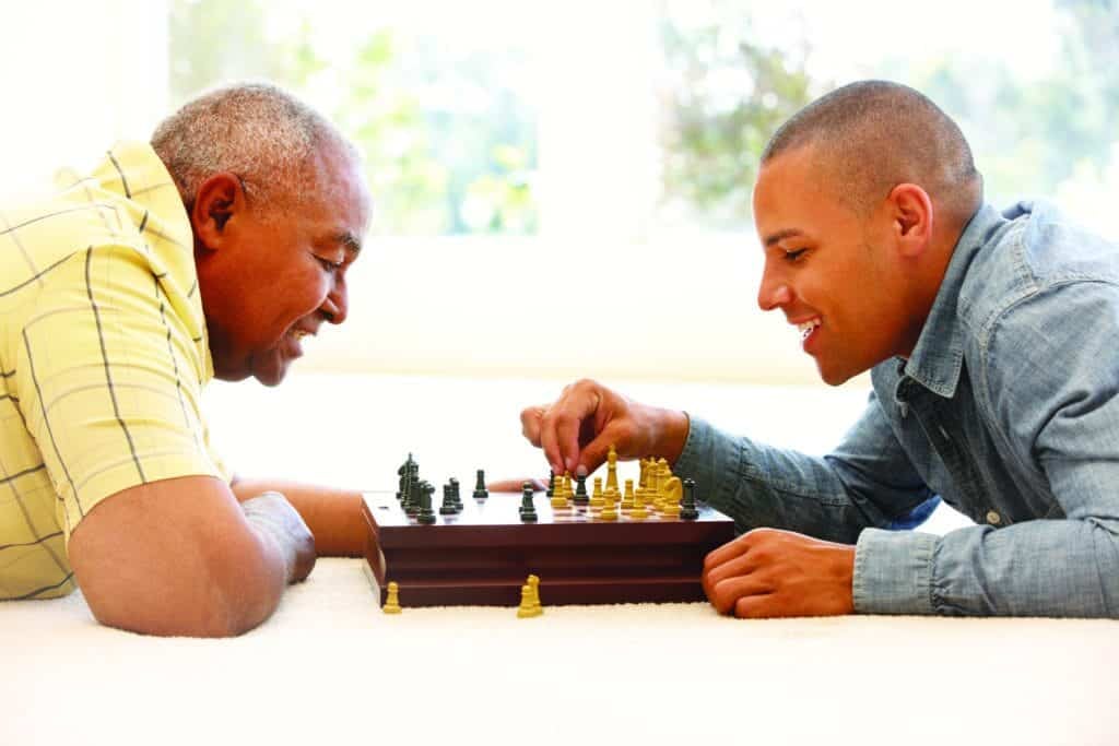 A man and his son are playing a game of chess enjoying the comfort in their home